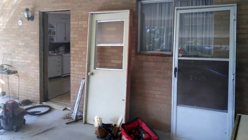 Old back door and storm door before the swap, tools on the patio