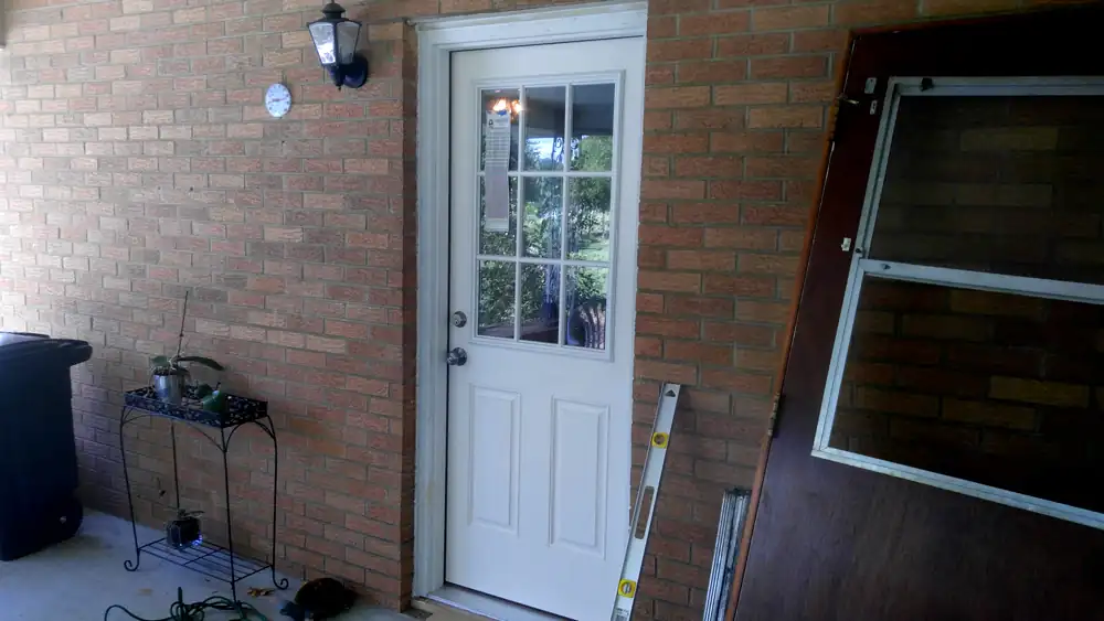 A new pre-hung half-lite back door set in a brick wall, level still leaning on the frame