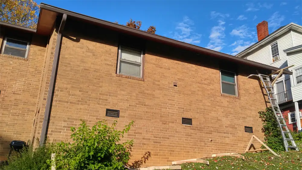 Brick house eave with the old fascia and gutter still up and a ladder against the wall