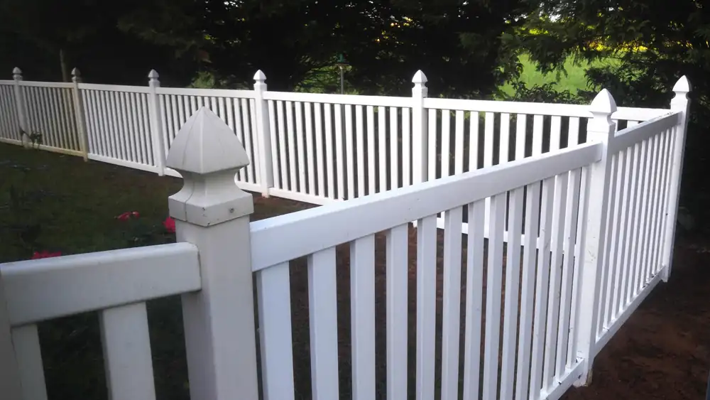 Repaired white vinyl fence with new posts running across a back yard