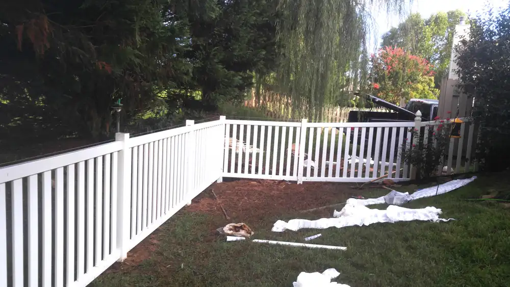 Run of vinyl fence across a yard with fence wrap lying on the grass