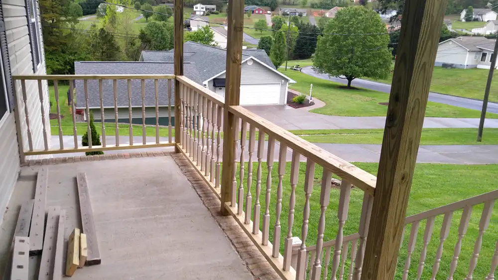 View along a rebuilt porch rail with new posts, looking out over the street