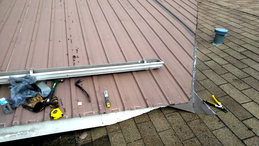 Metal roof meeting shingles at a rebuilt valley, with tools resting on the roof