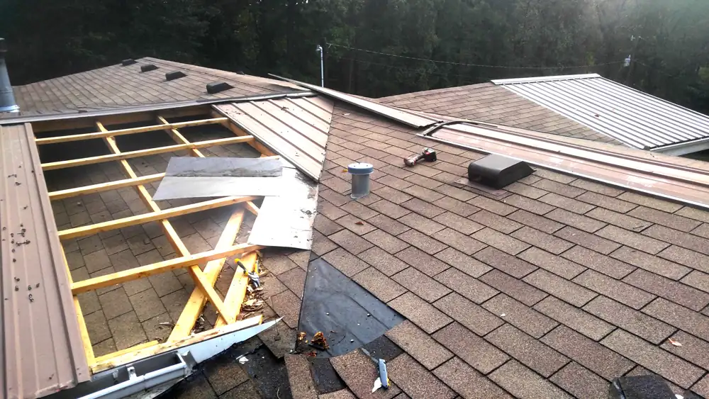 Shingles stripped back to new framing where a metal roof meets a shingle roof, mid-repair